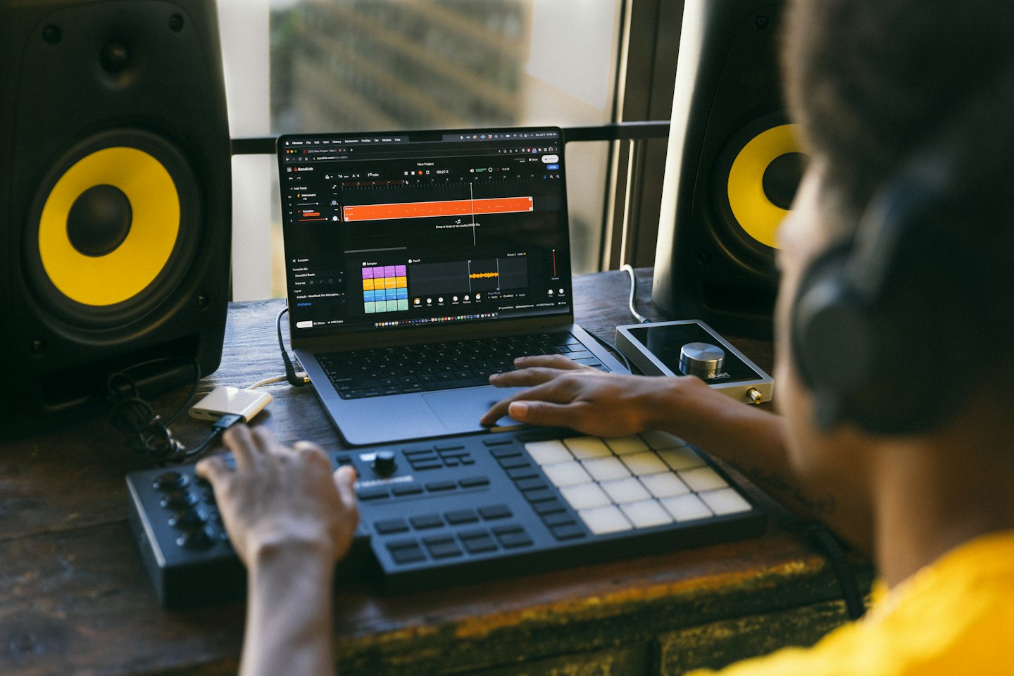 Person producing music on a laptop and MIDI controller with headphones on.