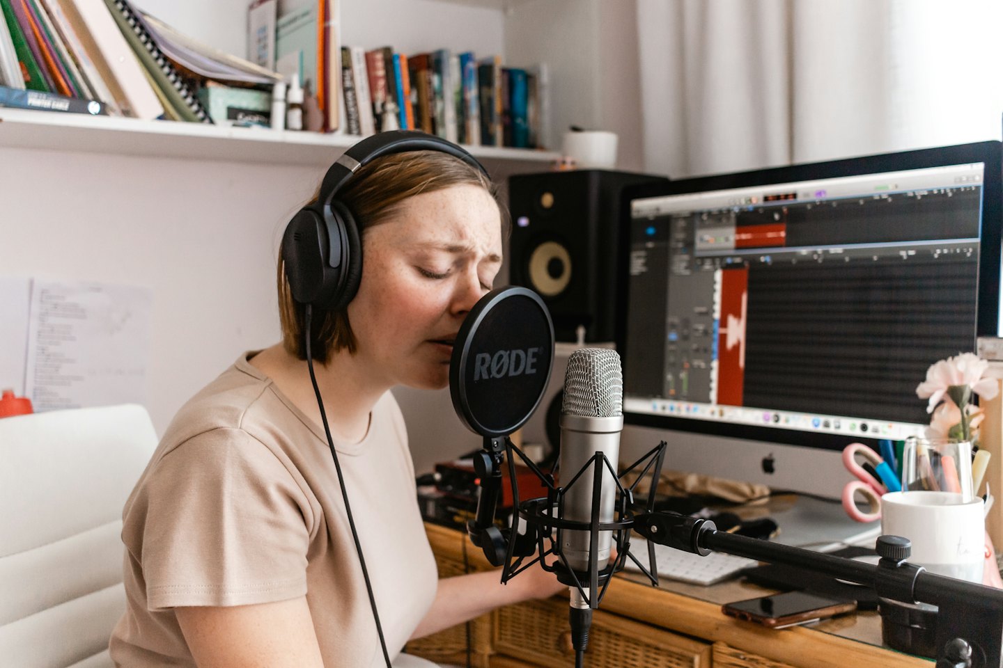 Woman records audio wearing headphones and singing into a microphone.