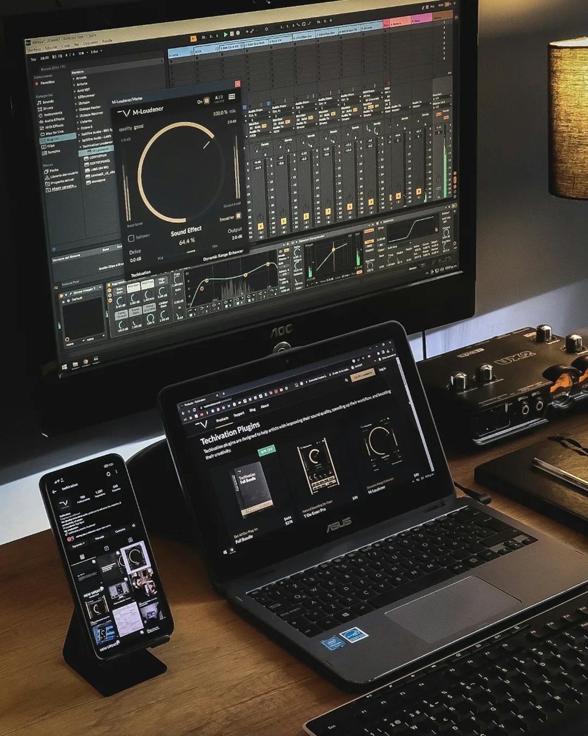 Music production equipment and screens sitting on a wooden desk.