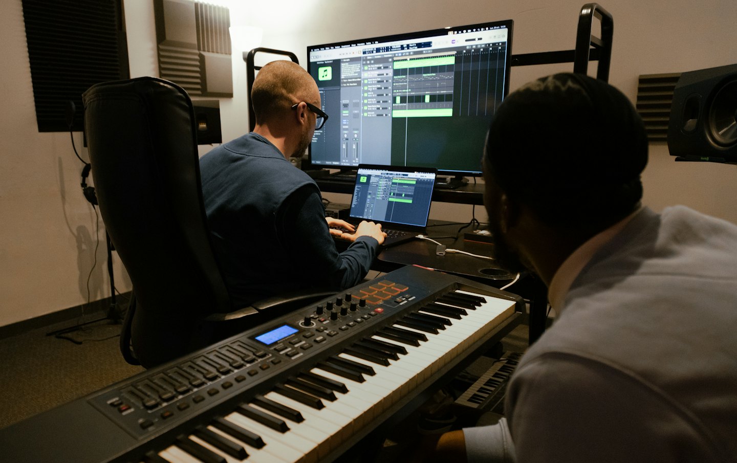 Two men working together in a music studio with a MIDI keyboard.
